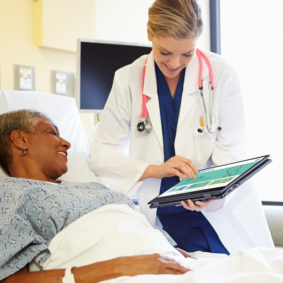 Un medico sorridente mostra informazioni a un paziente sdraiato su un letto d'ospedale tramite un ASUS ExpertBook in modalità tablet.