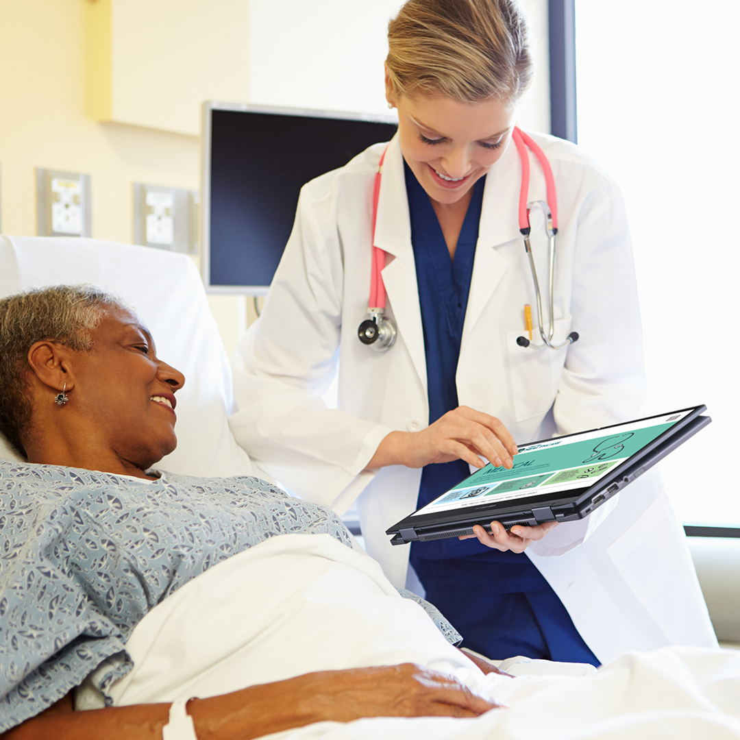 A doctor shows information to a  patient lying on hospital bed by ASUS ExpertBook in tablet mode with smile.