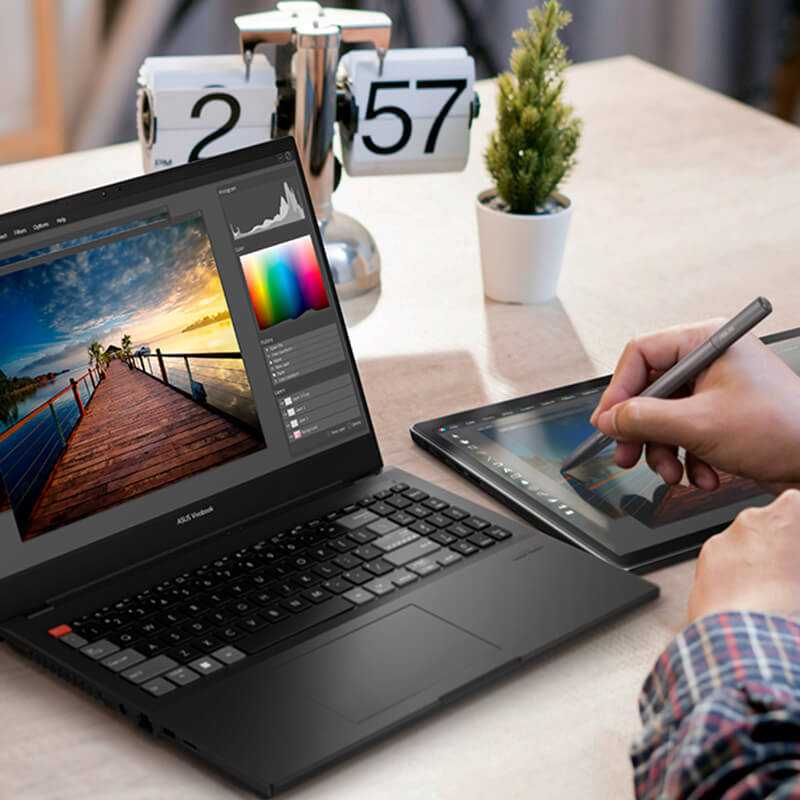a content creator using ASUS Vivobook Pro creator laptop and a pen tablet to edit photos at the desk with a camera next to the laptop