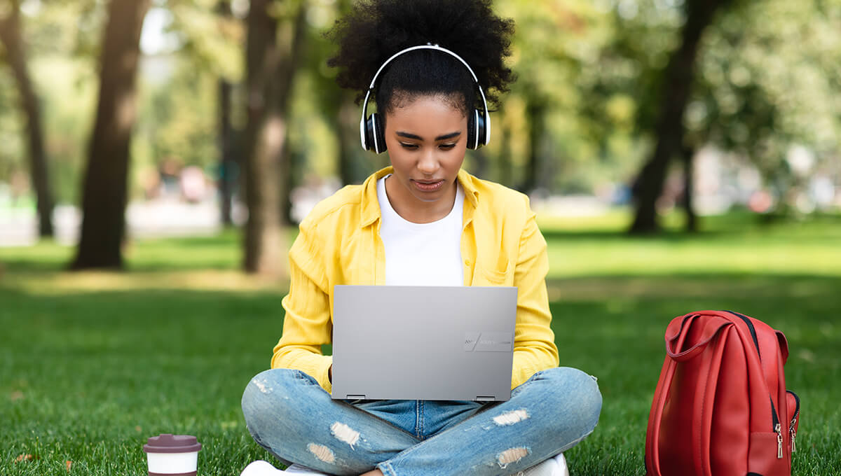 A young man is sitting in a chair using ASUS Vivobook S16 with several plants in the background.