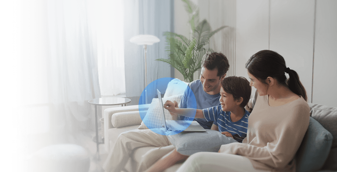 A family using laptops in the living room, with the laptop protected by a blue shield, showing how ASUS network security features secure every connected device.