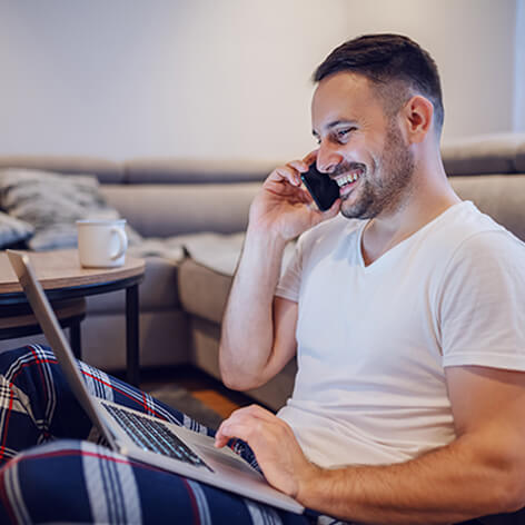 A man is using a laptop while talking on the phone, with a yellow circle on the laptop indicating a WiFi signal.