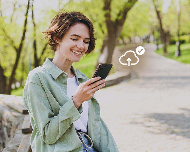 A smiling woman outdoors looking at her smartphone, with a cloud upload icon indicating auto security updates