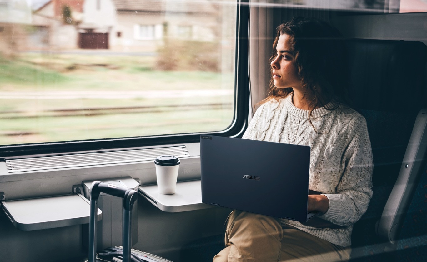 A woman sitting in the train is using ExpertBook B5 Flip OLED with all day long battery life up to 14hrs.