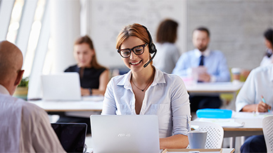 Eine weibliche Kundenbetreuerin in einem Büro, die ein Headset trägt und lächelt, während sie sich einen ASUS-Laptop ansieht.