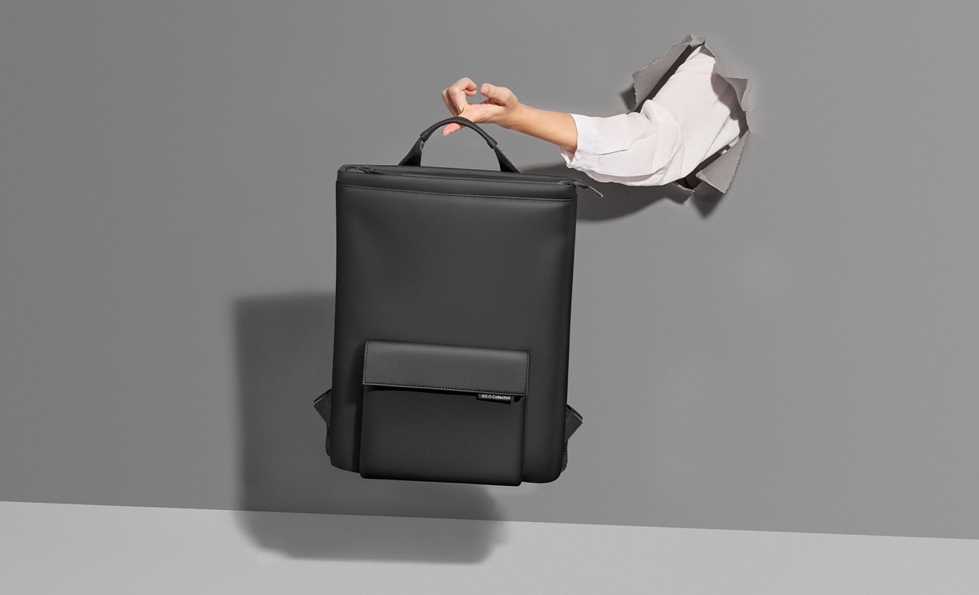 A disembodied arm extends through a wall, with an ASUS Vigour Backpack supported by a single finger on the hand.