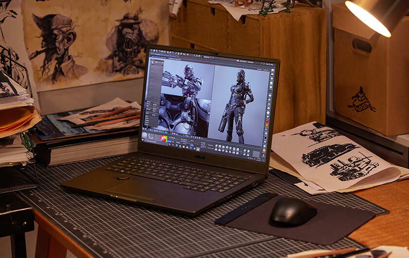 Le ASUS ProArt Studiobook Pro 16 OLED est placé sur une table dans un studio de création, à côté de plusieurs dessins de personnages.
