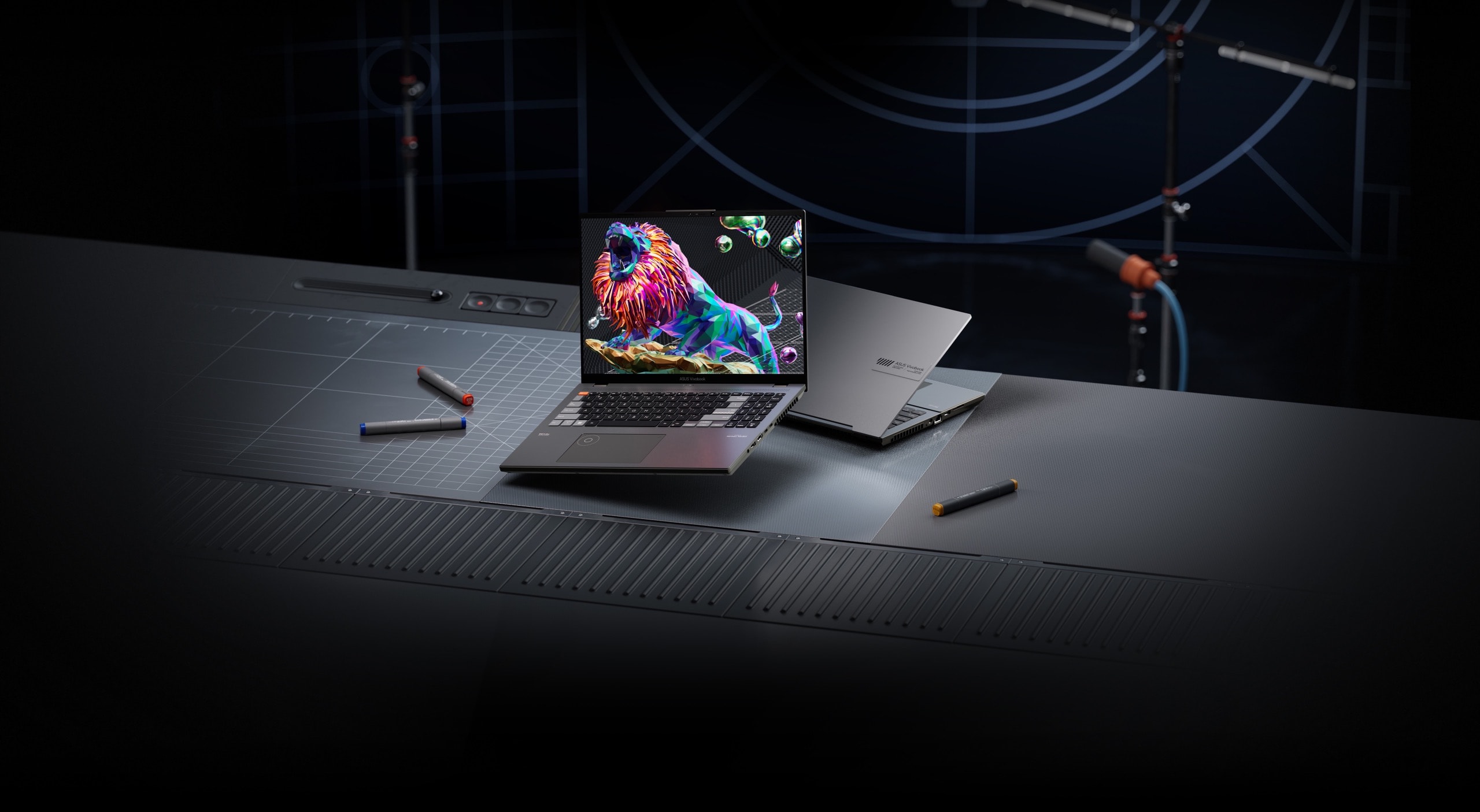 Чорно-срібляста модель Vivobook Pro 16X OLED показана на столі в студії звукозапису, а на екрані чорного ноутбука зображено рикаючий лев.