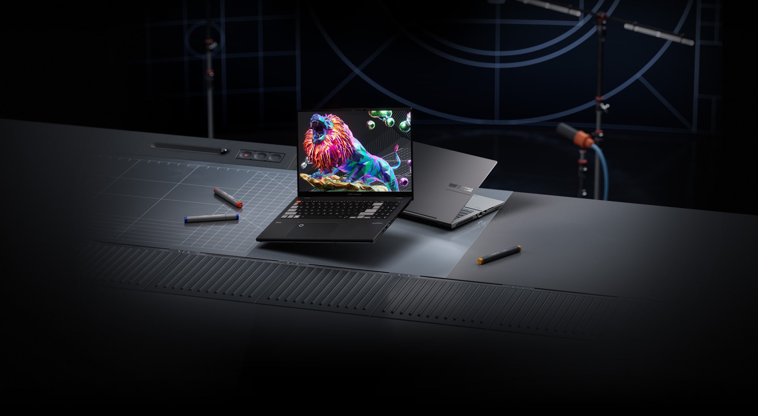 A black and silver Vivobook Pro 16X OLED model is shown on a recording studio desk with the black laptop in-screen showing a lion roaring