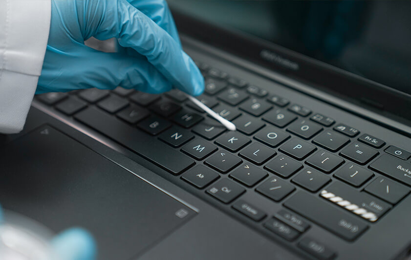 A person using an alcohol-dipped cotton swab to clean an ASUS Vivobook laptop keyboard area with antimicrobial coating