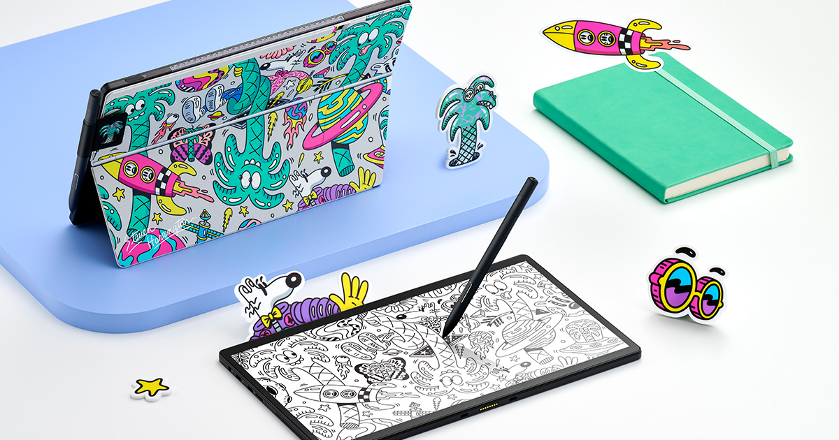 Two ASUS Vivobook 13 Slate OLED T3300 Steven Harrington edition 2-in-one laptops with detachable keyboards with colorful psychedelic art by Steven Harrington on the wallpaper and on the back stand cover with stickers and a matching-color notebook around