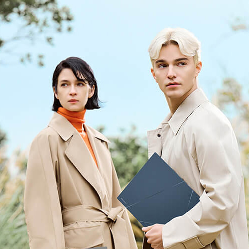 A man and a woman stand outdoors in a park-like setting, each holding an ASUS Zenbook.