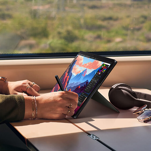 a content creator editing an image by using a stylus on the ProArt PZ13 laptop-and-tablet device on a table on a train