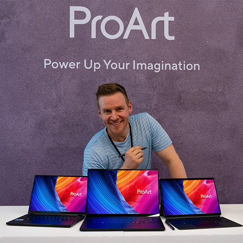 Jazza smiles holding a stylus behind three ProArt laptops.