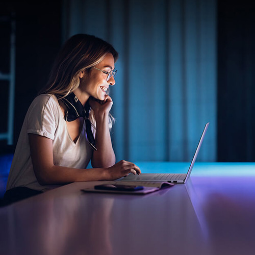 A smiling woman uses an ASUS Vivobook S 15 laptop in a dark room