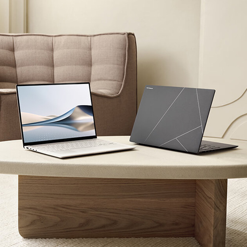 Two Zenbook S 16 laptops are placed on a beige colored table in a modern looking living room.