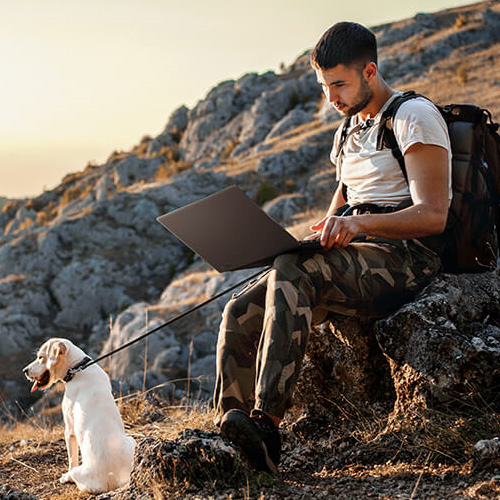 A man is using ProArt P16 while sitting on a rock beside a cliff.