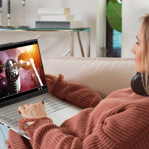 A young woman sitting on a pink sofa with an ASUS laptop on her lap, watching an online video