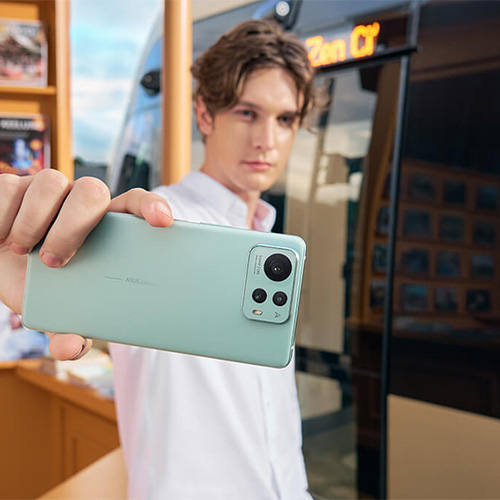 a man holding an ASUS Zenfone 12 Ultra (Sage Green), standing in front of a bookshelf.