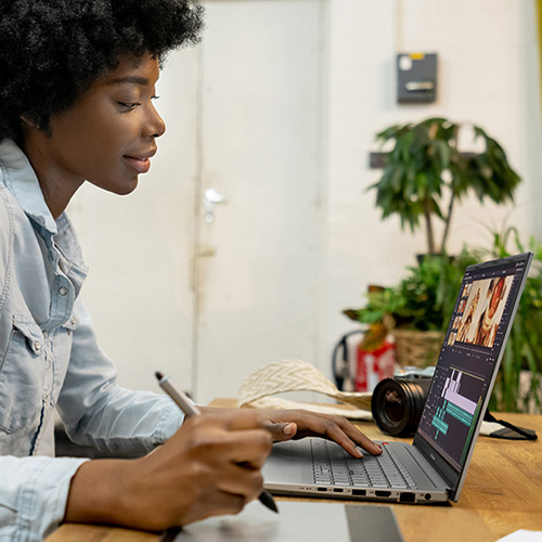 Девушка, сидя за деревянным столом, редактирует видео с помощью стилуса, графического планшета и ноутбука ASUS Vivobook Pro 15 OLED. За ноутбуком видна фотокамера.