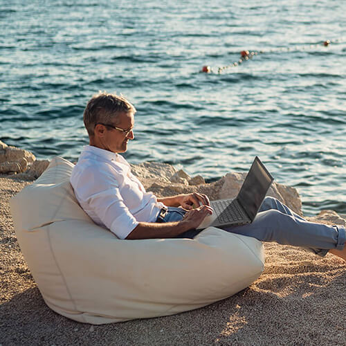 Мужчина средних лет на пляже пользуется ноутбуком ASUS Vivobook.