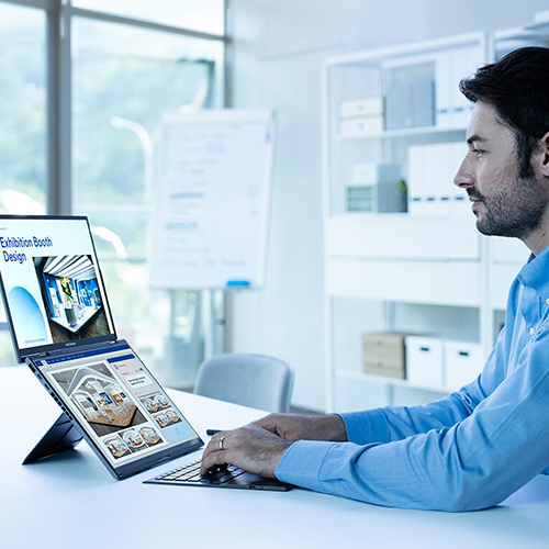 A man in a blue shirt is typing on Zenbook DUO with different information shown on the upper and lower screens.