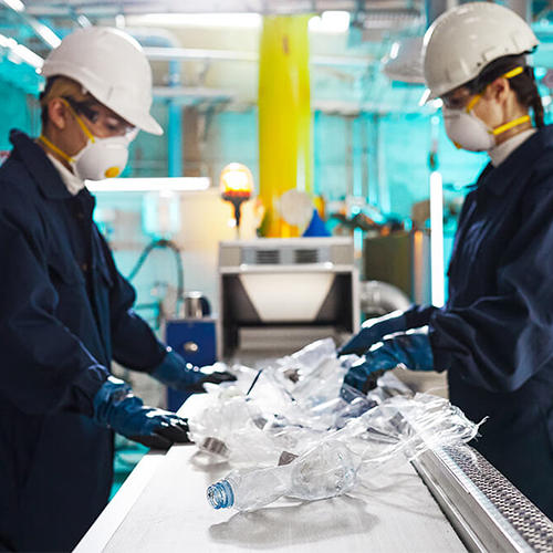 Мужчина и женщина в спецодежде работают на конвейере, сортируя пластиковые бутылки.