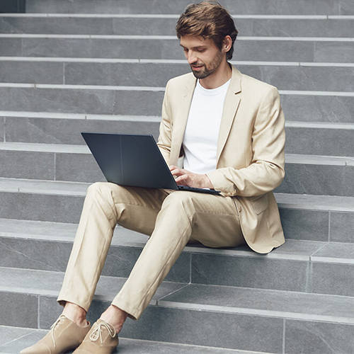 A man in a beige suit is using ASUS Zenbook 14 OLED on his lap while sitting on grey stone stairs.