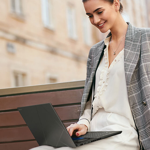 a young woman using ASUS Zenbook DUO laptop on her lap while sitting on a bench outdoors