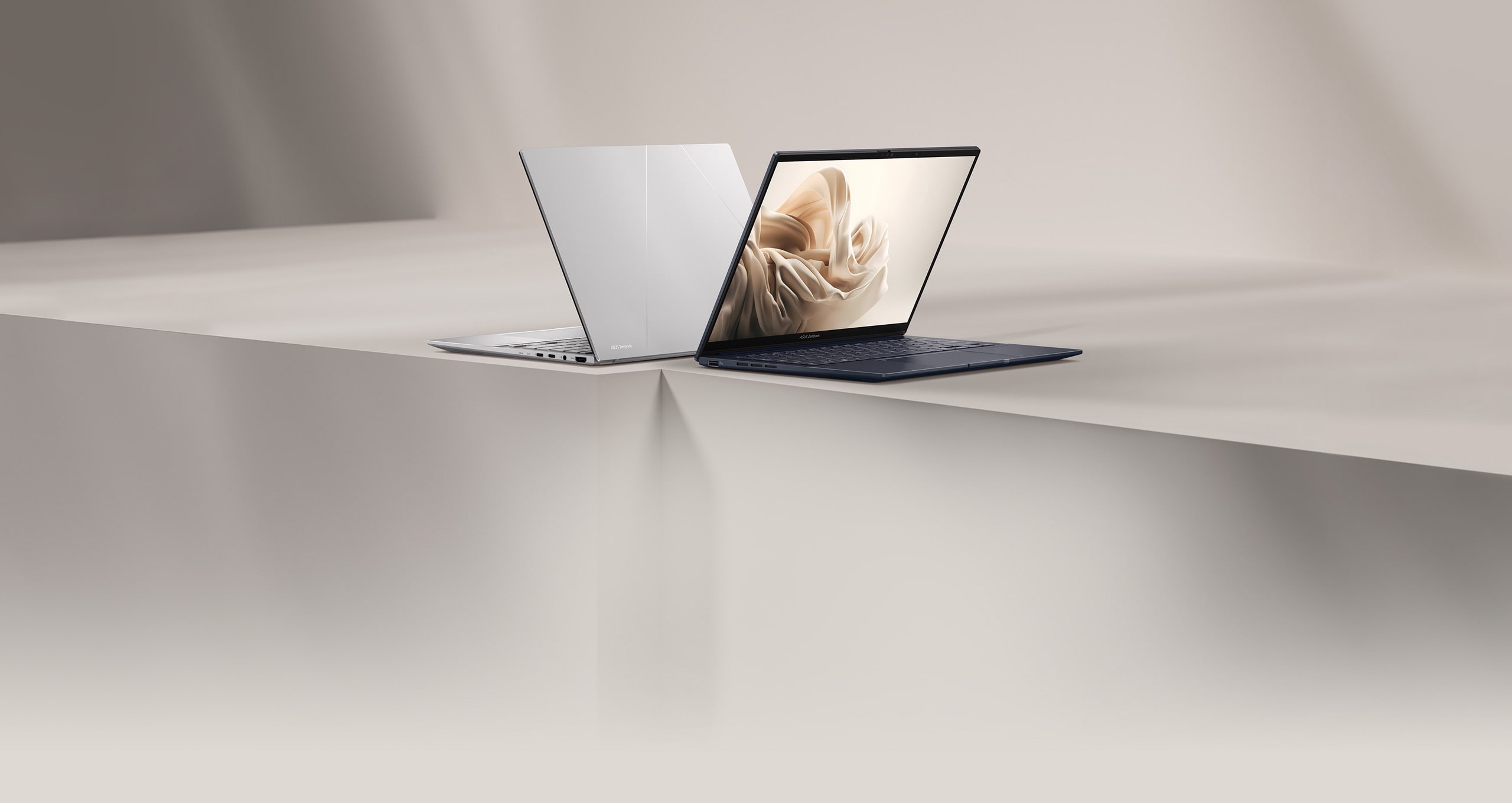 Zenbook 14 OLED i Ponder Blue og Foggy Silver placeret i et beigehvidt åbent rum med lys og nuancer.