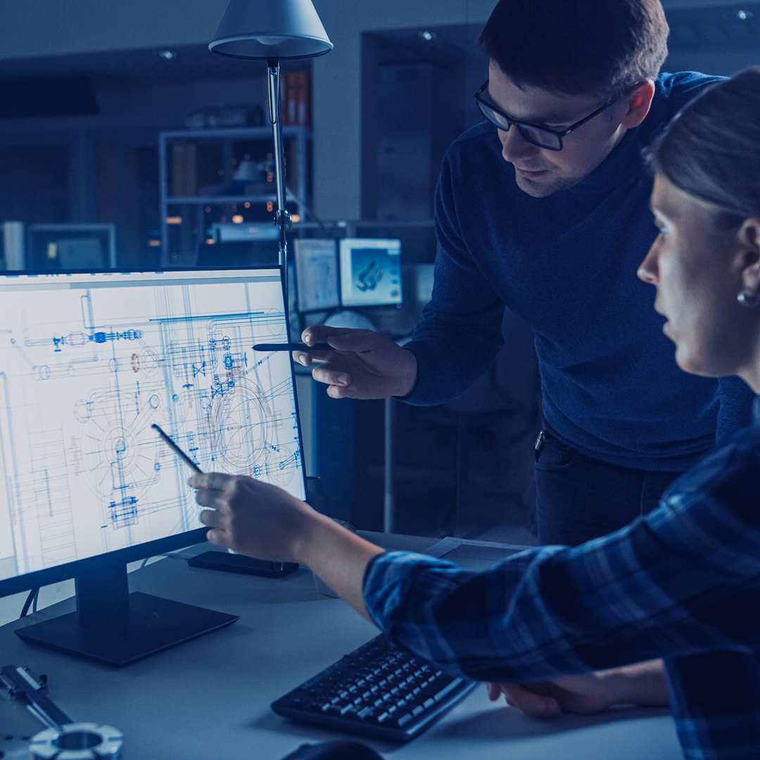 Two engineers discussing engineering drawings in front of computer screen