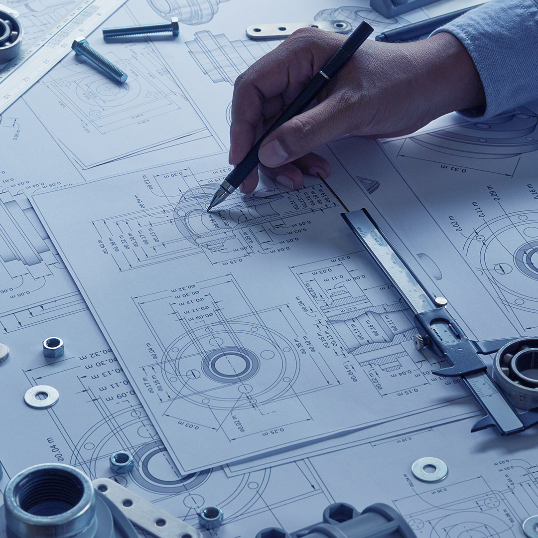 Engineer technician designing draws mechanical parts in a factory. Project blueprints and measuring bearings caliper tools are on the table.