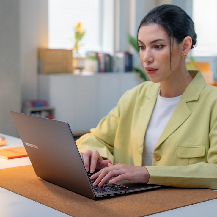 In a small home office, a young business female worker is working by an ExpertBook laptop at desk.