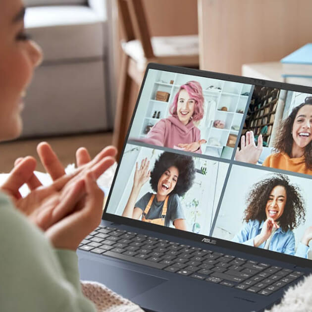 A woman is dressed in cozy home attire while she uses an ASUS Vivobook on a sofa.