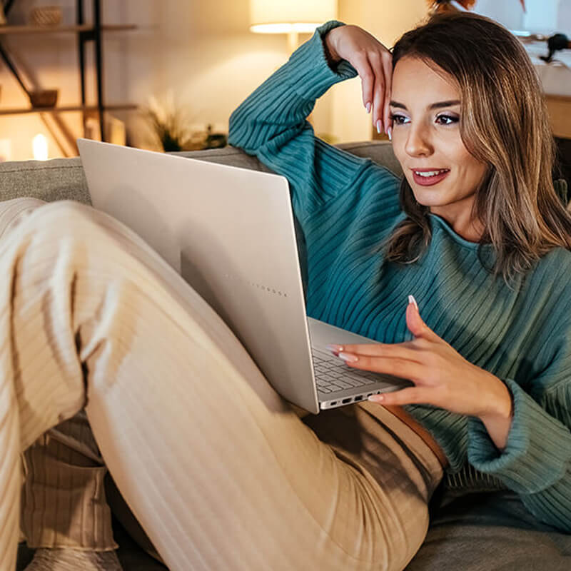 A young woman sits on the sofa while she uses an ASUS Vivobook S16 laptop