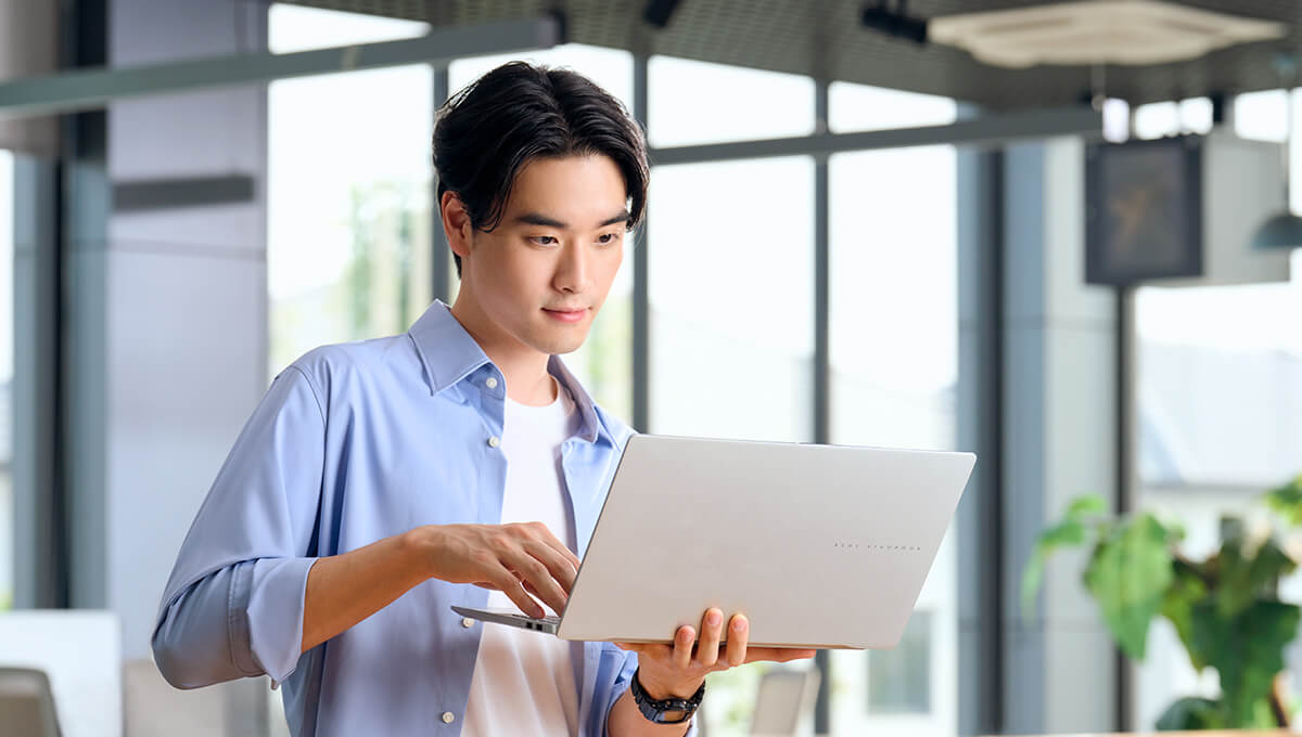 A man in a blue shirt is holding ASUS Vivobook S 15 with one hand and navigating the device with the other.