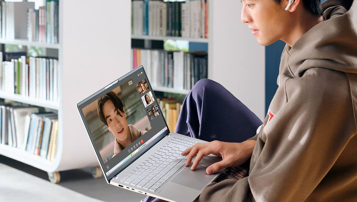 Een man in een bibliotheek voert een online videogesprek met behulp van zijn ASUS Vivobook.