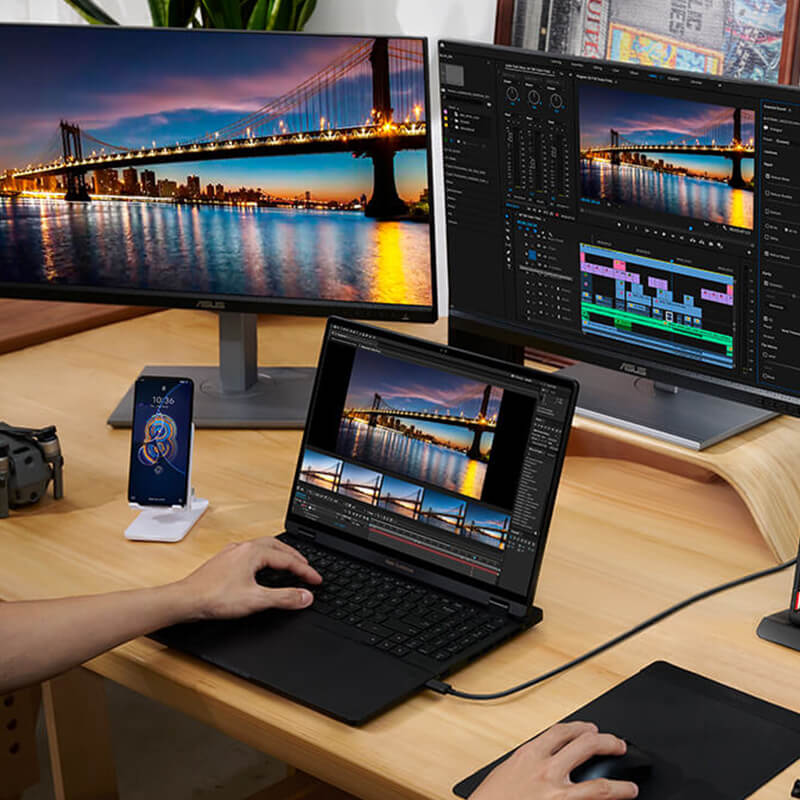 A laptop is put on the table with three monitors connected in front of it. Some of the screens show a stunning night view of the bridge, while others display video editing of the same bridge. There’s a Zenfone next to the laptop.