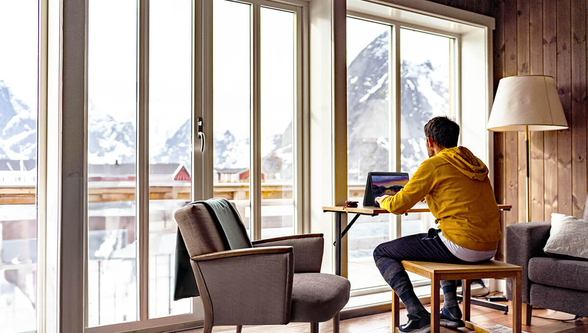 A man in a yellow jacket is using the ProArt PX13 laptop in tent mode. He is in a wooden cabin in some snowy mountains.
