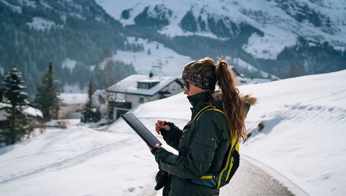A woman is holding the ProArt PZ13 detachable laptop in one hand while scrolling with the other. She is in the snowy mountains in the middle of a trail.