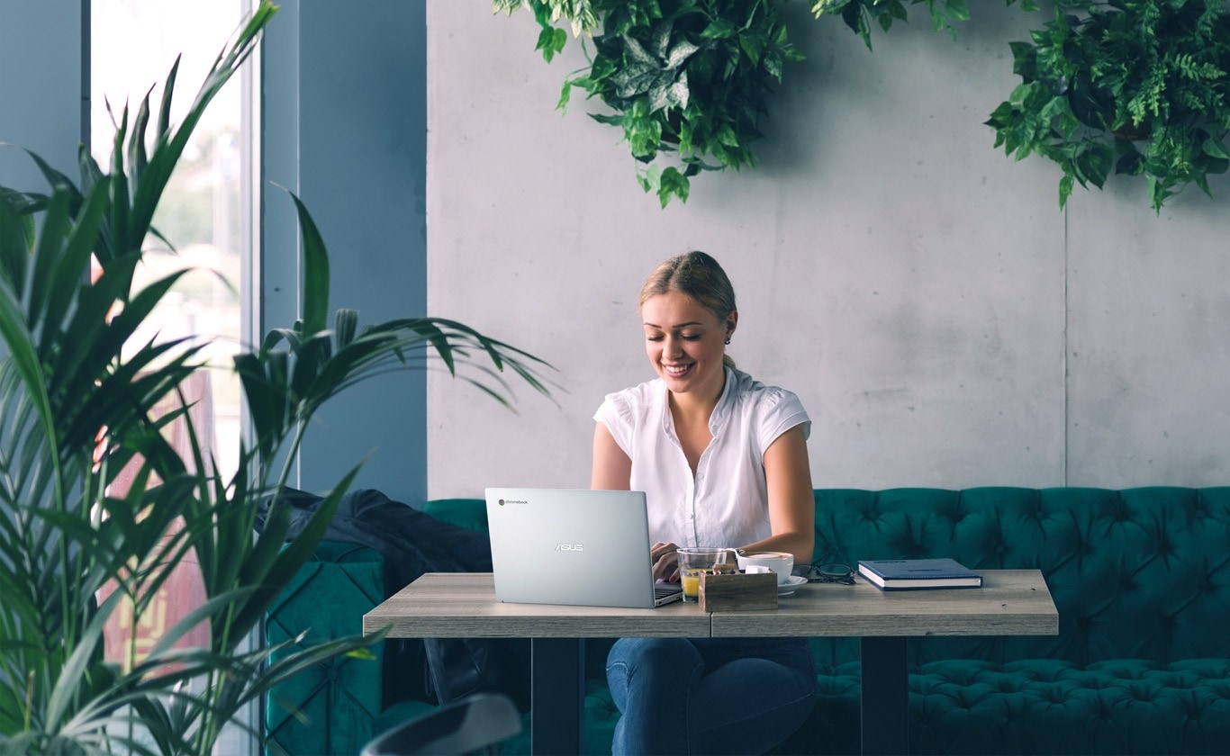 Women sitting in café sofa with ASUS Chromebook CX1101, surrounded by greenery 