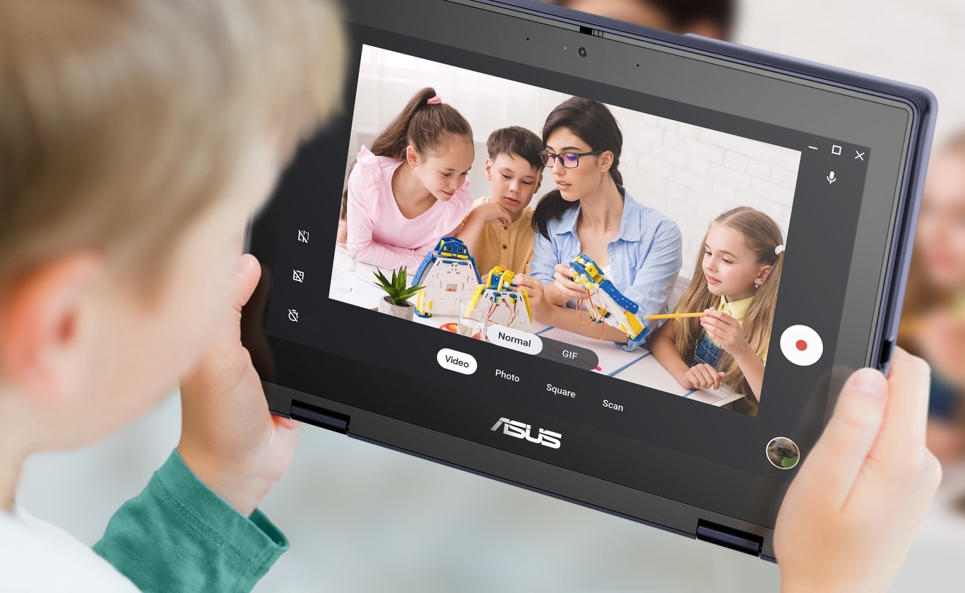 Dieťa drží notebook ASUS Chromebook CR11 Flip v režime tabletu a vyhotovuje fotografie troch ďalších študentov pracujúcich na projekte spolu s učiteľkou.