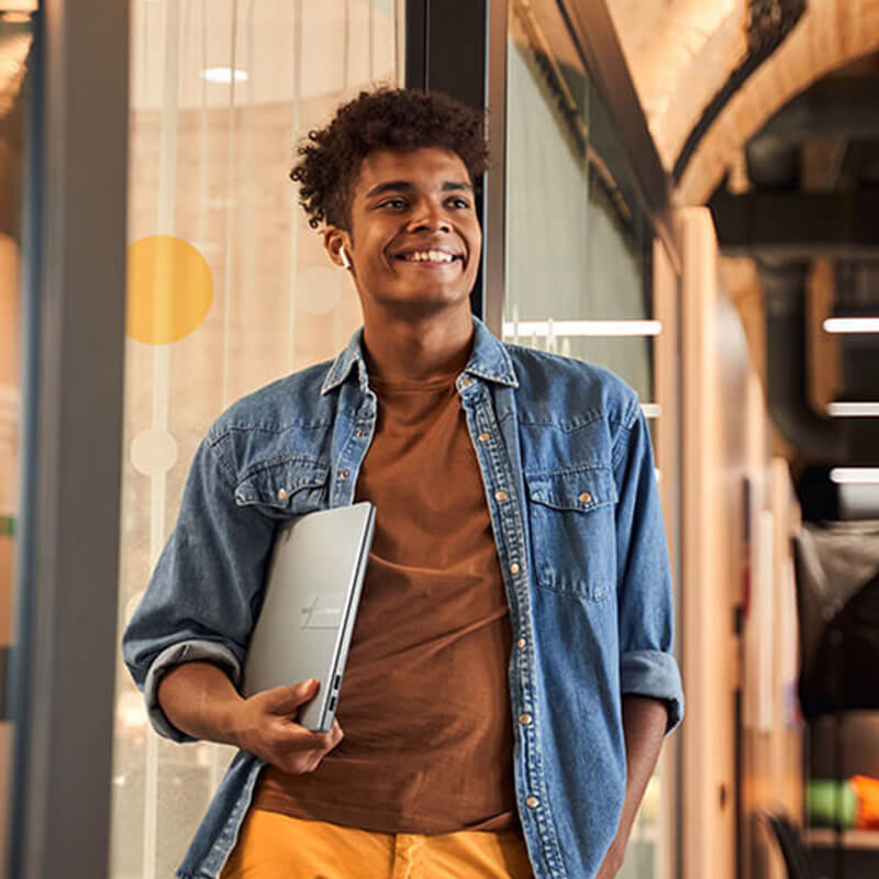 Un jeune homme portant l'ASUS Vivobook 14 Pro OLED dans ses mains tout en marchant dans le couloir de l'université.
