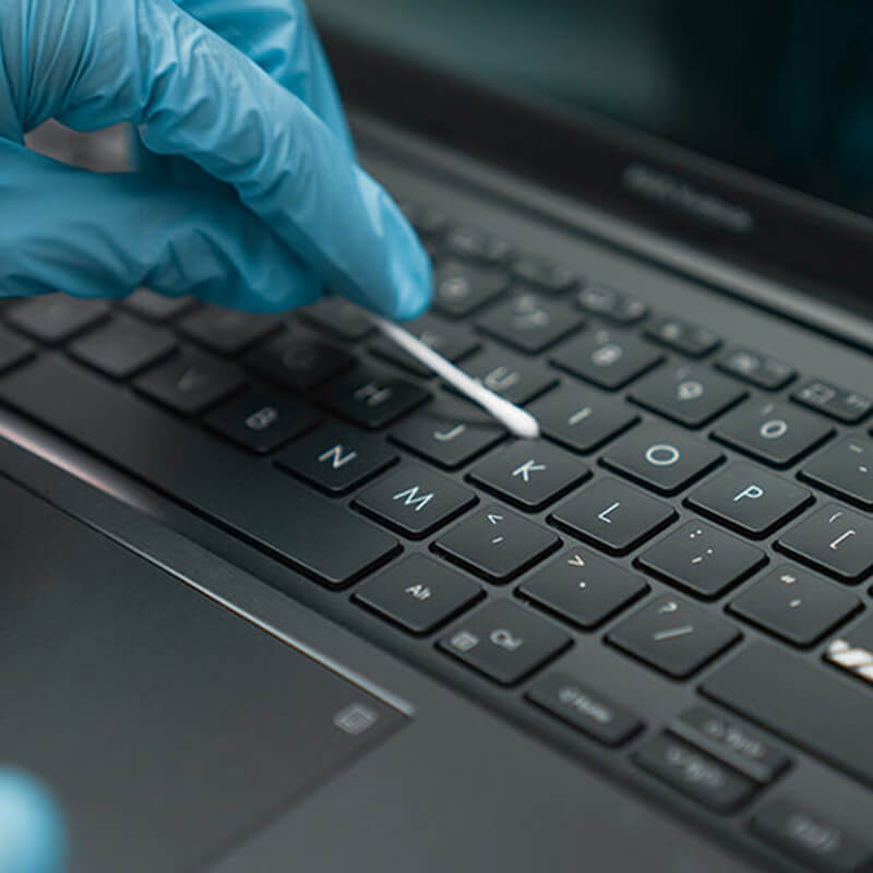 Una persona que utiliza un hisopo de algodón humedecido en alcohol para limpiar el área del teclado de una computadora portátil ASUS Vivobook con revestimiento antimicrobiano