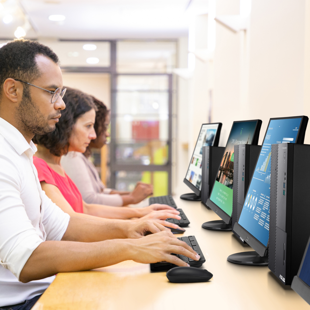 Trois personnes utilisent des ordinateurs de bureau dans un lieu public.