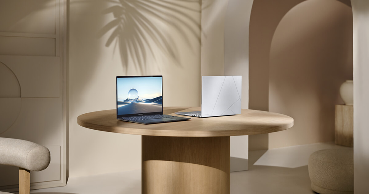 Two Zenbook 14 OLEDs are placed side by side on a round wooden table.