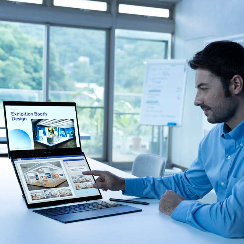 A man in a blue shirt is pointing at the screen of Zenbook DUO in a white meeting room. The screen on top is displaying his main project while the screen on the bottom is displayed with split windows.