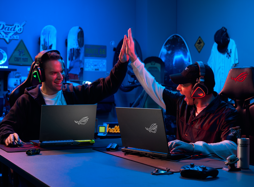 Two people sitting at a table, both with a Strix G15, high-fiving.
