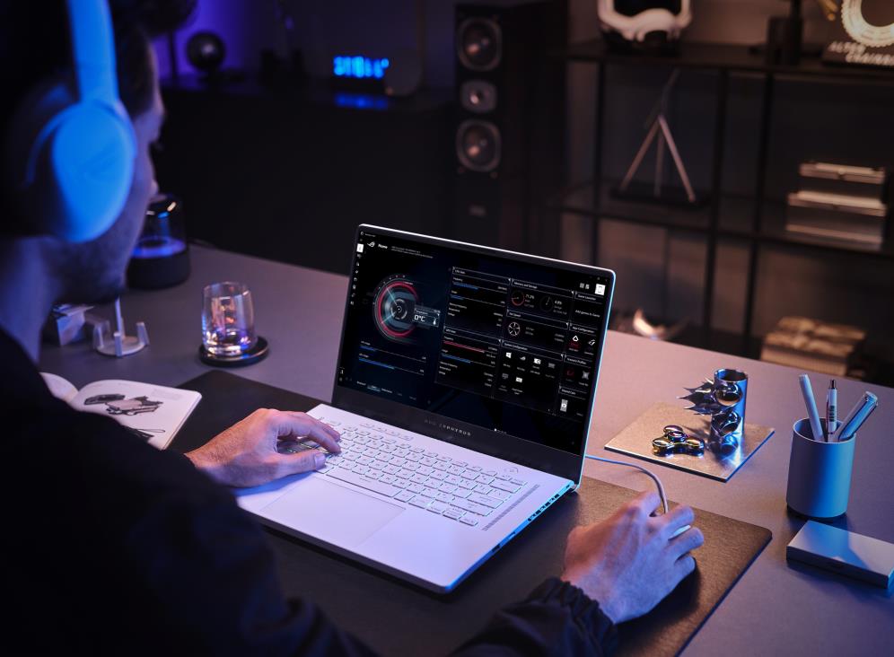 Person uses a white Zephyrus G15 with white peripherals while seated at a table, with Armoury Crate open on screen.