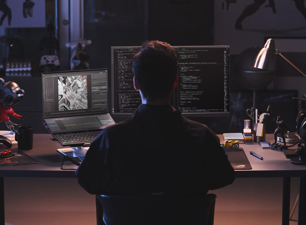 Person seated at a table with the Zephyrus Duo 16 and an external monitor, working on animation and coding projects simultaneously.